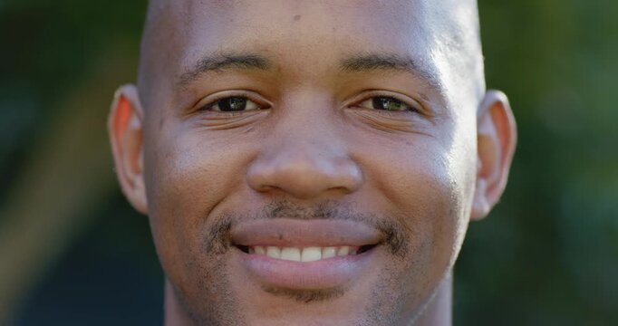 Adult African man facing camera, smiling gradually from neutral to broad grin in park, showing joy