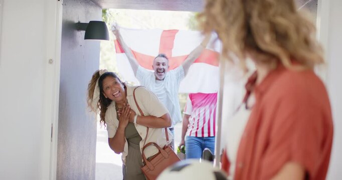 Diverse friends arriving to visit woman waving flag resident holding ball opening arms hugging