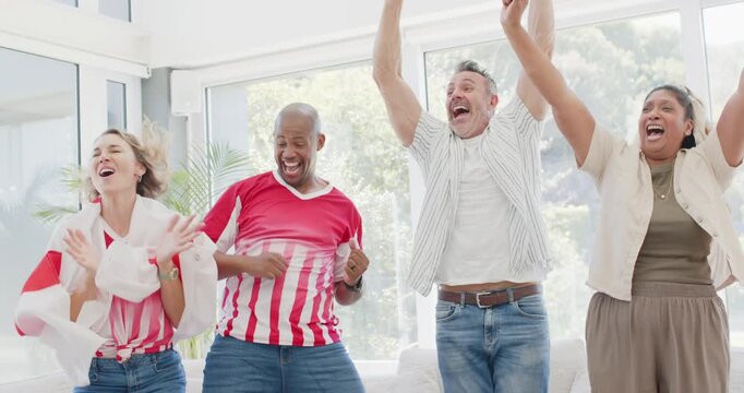 Diverse friends in living room cheering after off-camera goal, standing, hugging on sofa, chips