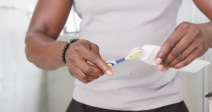 Adult African American man aligning brush under cap squeezing tube at sink starting brushing teeth