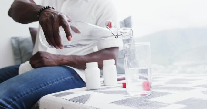 African American man preparing to take meds, polo, pouring water from bottle into glass on balcony