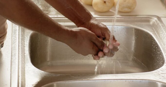 African American man reacting to running faucet, picking and washing potato at sink for cooking