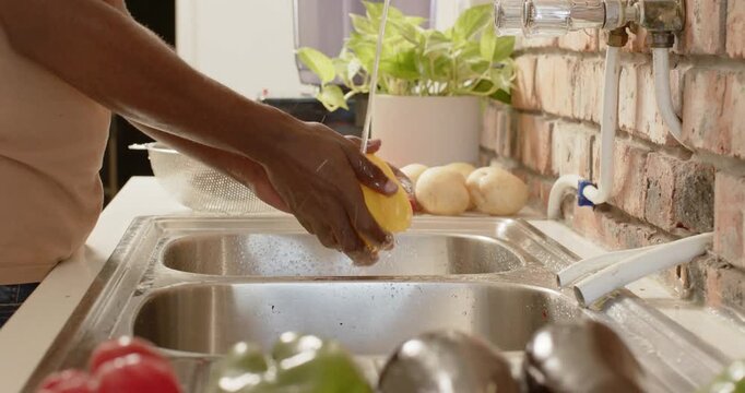 African American man washing yellow-green peppers under tap at kitchen sink with colander to cook