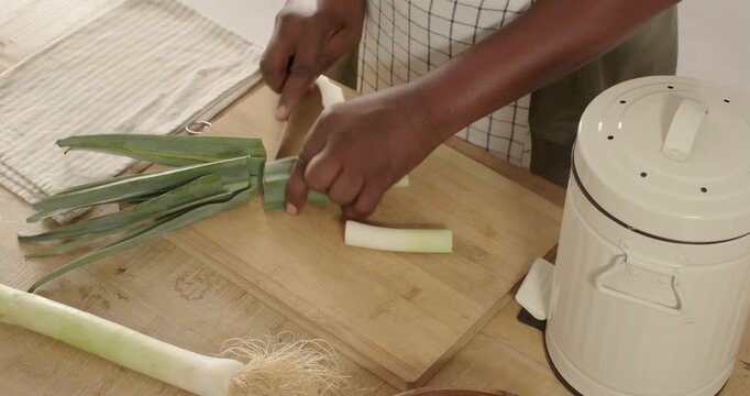 African male cook trimming leek tops into compost, slicing stalk on board with knife, copy space