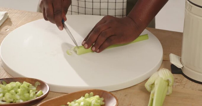Celery stalks are being sliced on round cutting board with blue knife, diced piles forming