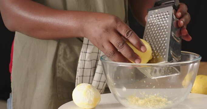 Mid-adult man holding halved lemon, zesting on box grater into glass bowl in kitchen for flavor