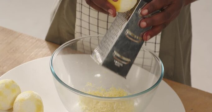 Mid adult male holding peeled lemon, using grater, grating zest into glass bowl at kitchen counter