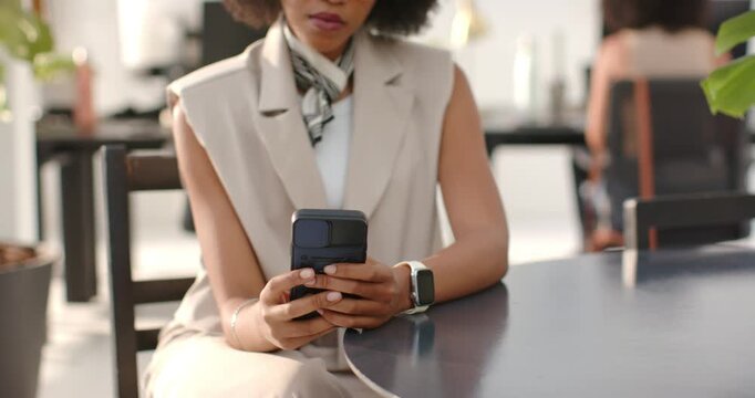 African American woman checking smartphone after alert while scrolling and reading at round table