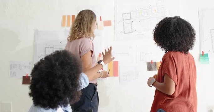 Diverse women team checking plans swatches pinned at studio after seated woman gesture with pencil