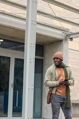 African American man standing at entry holding smartphone wearing beanie with bag, copy space © wavebreak3