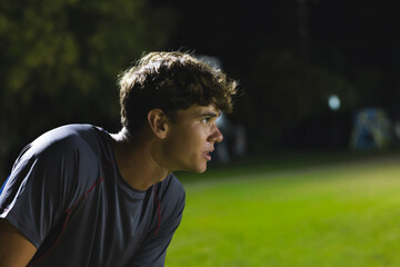 Leaning forward, man in early 20s observing play on grass pitch at night, wearing athletic shirt © wavebreak3