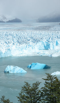 Panoramic view of Perito Moreno Glacier with floating blue icebergs in a glacial lake under overcast sky in Patagonia, Argentina