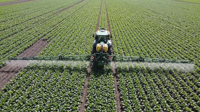 Aerial view of a tractor spraying fertilizer on green crops in a field