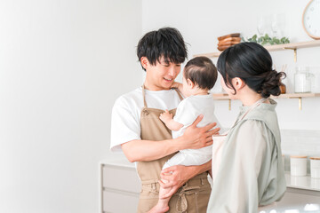 Fototapeta premium A couple in aprons holding their baby in the kitchen, a family