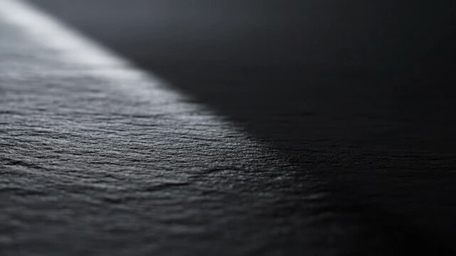 Dark textured stone surface with a dramatic diagonal light beam casting a deep shadow across the frame