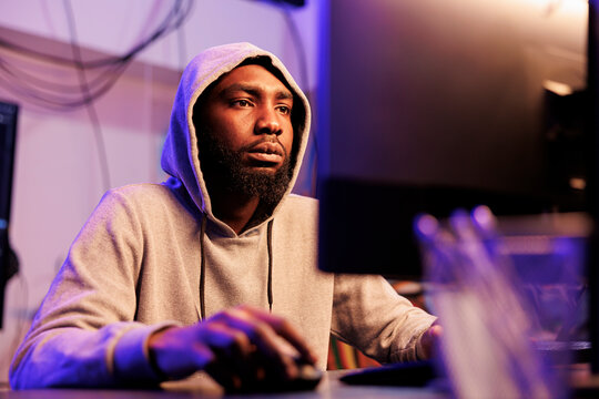 African american hacker coding virus malicious software on computer and breaking law. Criminal in hood using stolen password to breach company server and commit online fraud