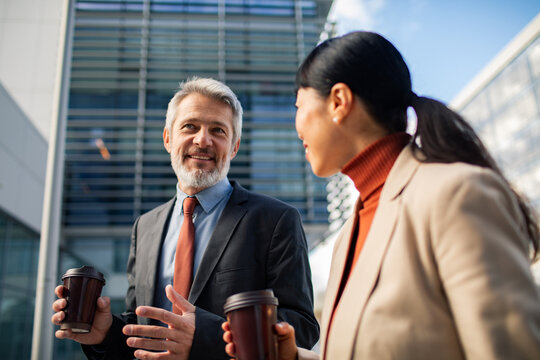Two business professionals chatting with coffee outside office building
