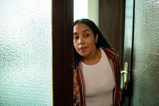 Curious woman peeking through a doorway at home