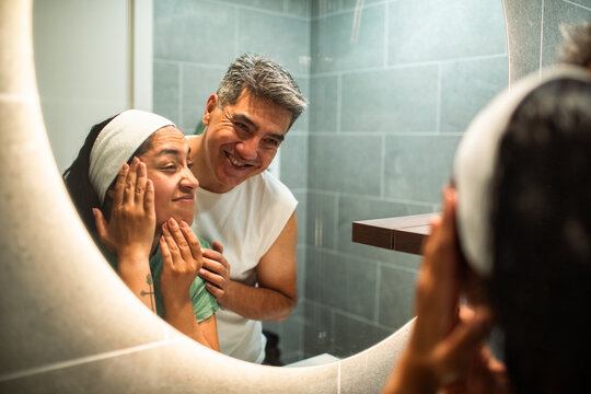 Smiling couple practicing skincare routine in home bathroom mirror