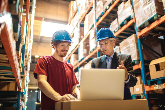 Two workers using a laptop in a warehouse aisle