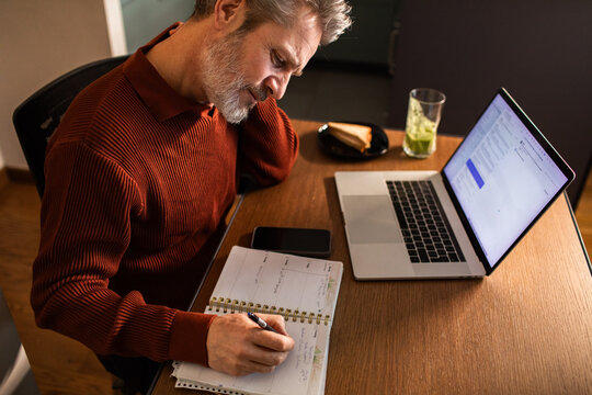 Mature man writing in planner at home office desk