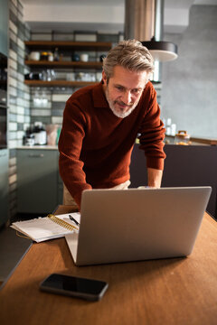 Middle-aged man working on laptop at home kitchen table