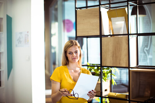 Confident young businesswoman holding document in modern office