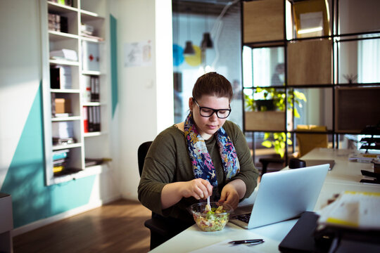 Young woman eating salad at desk in modern office