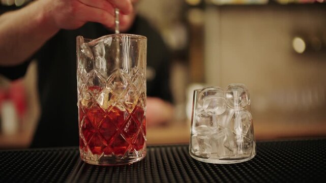 Close up of a bartender stirring a cocktail with ice in a crystal mixing glass