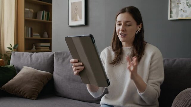 Medium shot of cheerful, smiling Caucasian girl chatting to friend on video call with digital tablet, losing network connection, swiping to internet configuration, swearing at signal outage