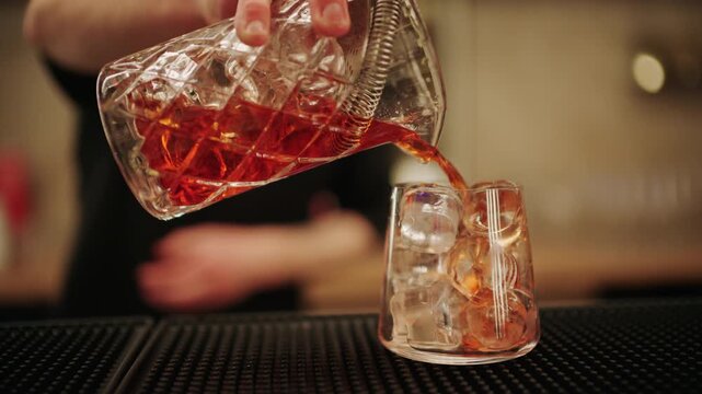 Bartender pouring a freshly mixed red cocktail into a glass filled with ice