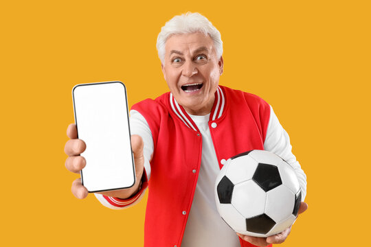 Happy senior man with soccer ball and blank mobile phone on yellow background. Sports bet concept