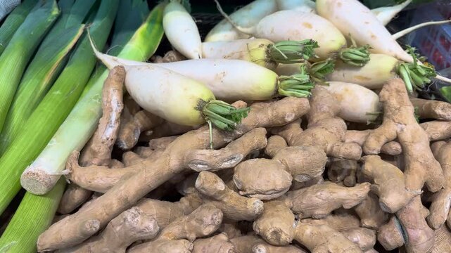 Fresh ginger and radishes at a local market in the afternoon with green onions in the background