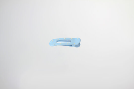 Light soft blue hair clip rests on plain white surface. Minimalist design catches eye with clean lines, with decorative dot details,  simple curved design and secure clasp isolated on white background