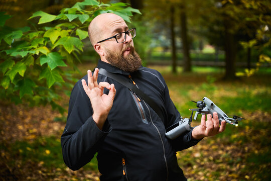 Man gestures OK sign while holding drone and controller. Bearded man satisfied with setup in park, expressing approval and confidence, concept of success, ease of use and technology