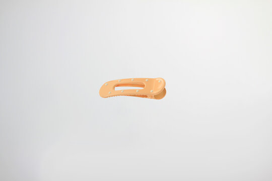 Light soft orange hair clip rests on plain white surface. Minimalist design catches eye with clean lines, with decorative dot details, simple curved design, secure clasp isolated on white background