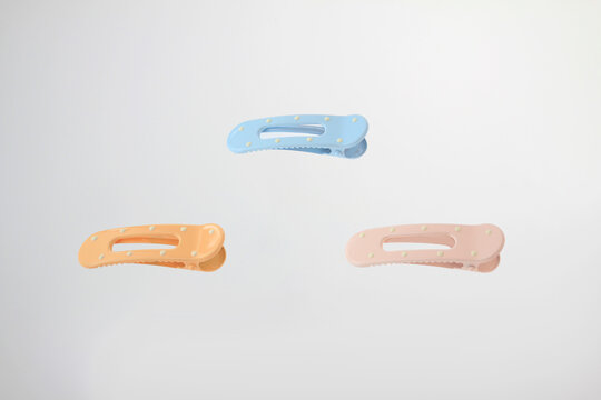 Pastel colored hair clips float against a clean white background. Minimalist plastic hair accessories in soft blue, peach, and pink colors with decorative dot details arranged in balanced composition 