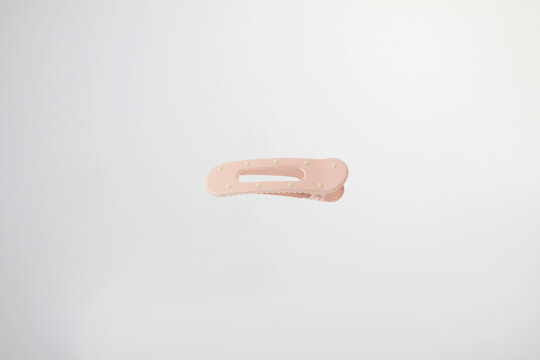 Light soft pink hair clip rests on plain white surface. Minimalist design catches eye with clean lines, with decorative dot details, simple curved design and secure clasp isolated on white background