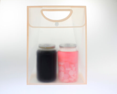 Clear bag holds two glass jars. One jar contains coffee. The other contains colorful pink fruit drink ice.  Transparent frosted plastic bag softly blurs the contents, isolated on white background. 