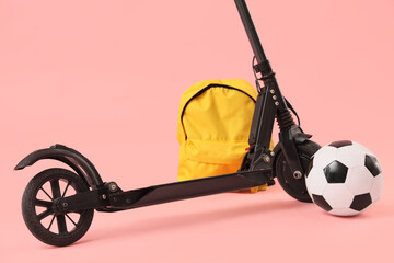 Modern electric scooter with backpack and soccer ball on pink background, closeup