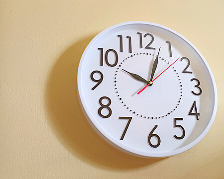Close-up of a white wall clock against a yellow backdrop. The wall-mounted white wall clock is in place. Modern minimalist white and black clock on yellow wall. best template for quote background.