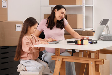 Fototapeta premium Working pregnant mother and her little daughter using calculator in warehouse