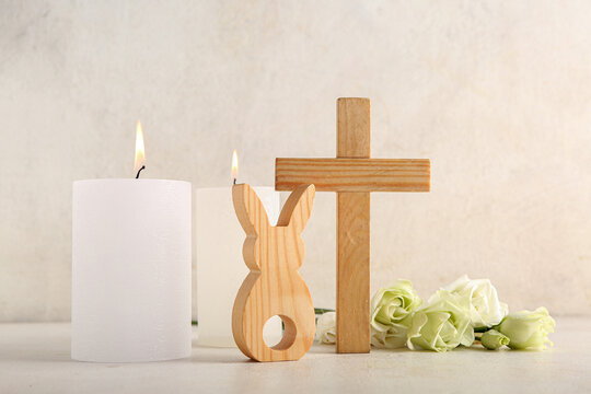 Wooden cross with burning candles, bunny and eustoma flowers on white grunge background. Easter celebration