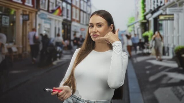Woman holding a red vaporizer and making a call me hand gesture on a busy street; playful invitation.