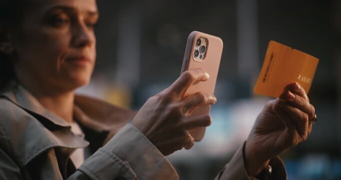 Young Woman in Airport Terminal, Carefully Cross Referencing Data Between Paper Ticket and Phone. Organization, Travel Planning, and Reliability of Digital Check in Services in Modern Aviation.
