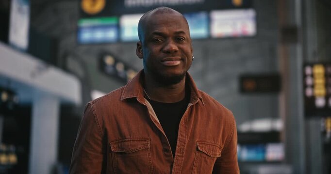 Portrait of African American Man Stands Peacefully in Center Crowded Departure Hall. While Other Passengers Move Quickly Around, Guy Remains Still and Composed, With Gentle Smile Playing on Lips.
