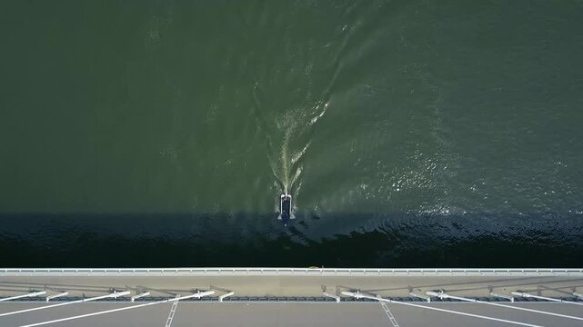 A black and white speedboat passes through across under a busy car bridge in Budapest, Megyeri
