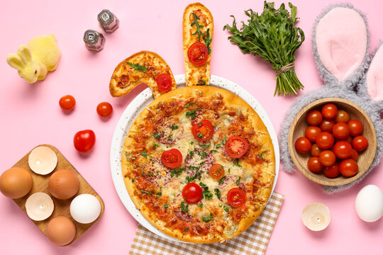 Tasty Easter pizza with ears, eggs, arugula and bunny on pink background