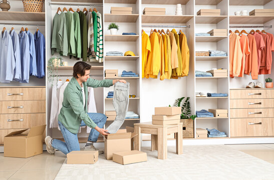 Handsome young man unpacking wardrobe boxes with stylish clothes in dressing room