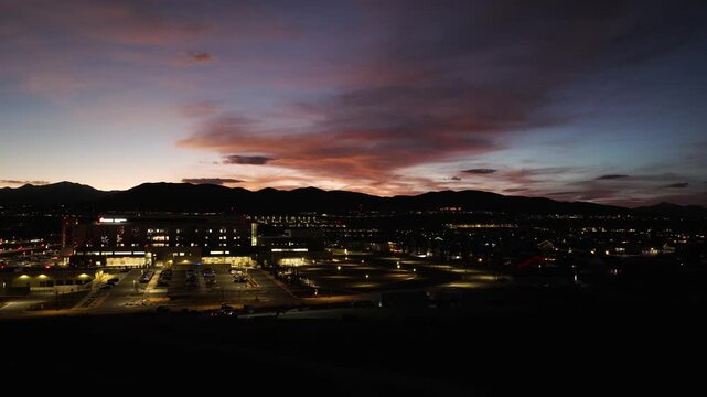 Silicon Slopes tech campus and commercial buildings in Lehi Utah glowing at dusk with Wasatch Range mountain backdrop and expanding urban grid under vivid sunset sky, aerial pullback reveal